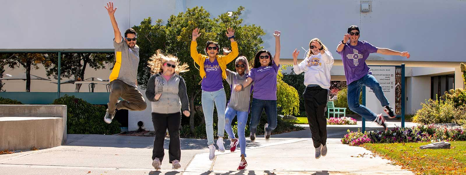 Students outside jumping with hands in air and smiling at camera